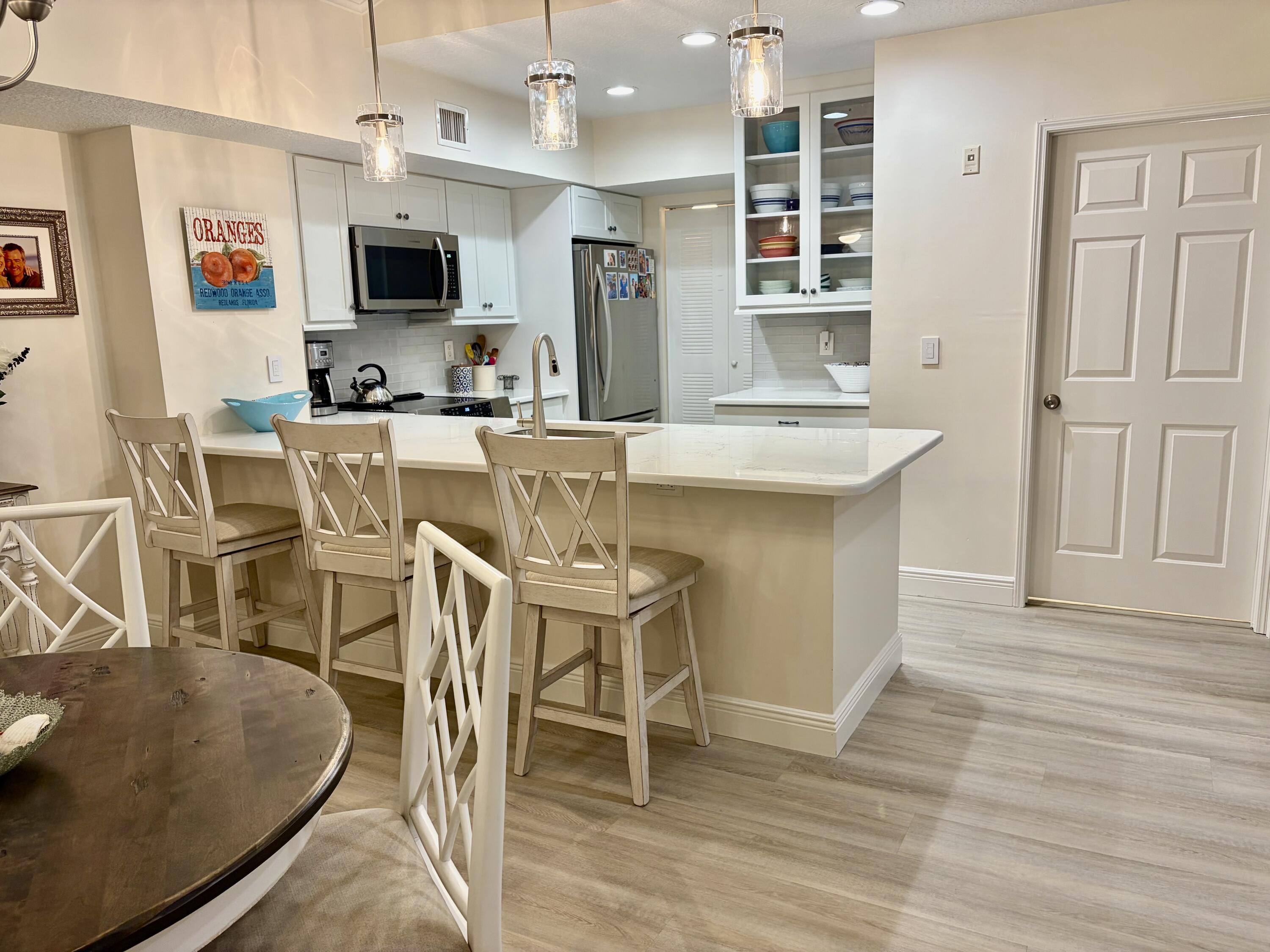 242 Village Boulevard, Unit 2304 Tequesta, FL 33469 - Photo 6 of 34 a kitchen with stainless steel appliances granite countertop a stove top oven a sink a dining table and chairs with wooden floor