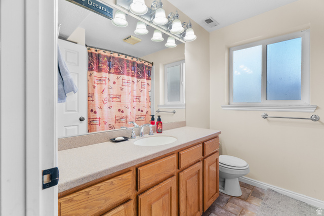 5727 South 3550th Street West Roy, UT 84067 - Photo 30 of 49 Full guest bathroom featuring a light-toned countertop, wood-finish cabinetry, an integrated sink with chrome faucet, and a toilet