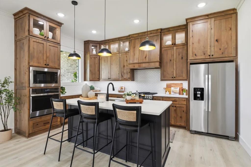 1310 Benjamin Trail Van Alstyne, TX 75495 - Photo 5 of 27 Kitchen featuring stainless steel appliances, glass fronted cabinets, a kitchen breakfast bar, light wood-style floors, and a center island with sink