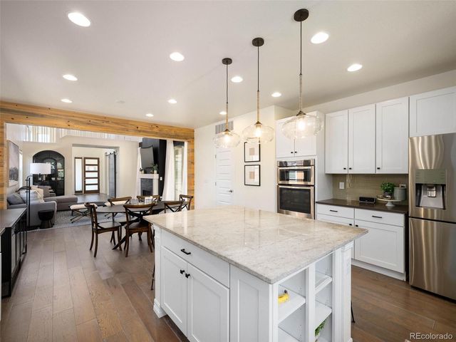 a kitchen with stainless steel appliances kitchen island granite countertop a stove a refrigerator a kitchen island a dining table and chairs with wooden floor