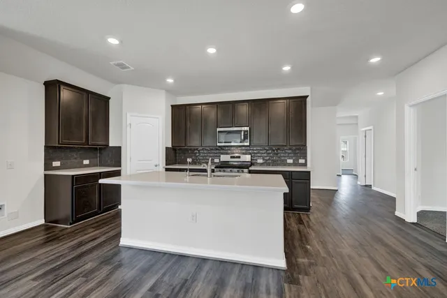 a kitchen with stainless steel appliances kitchen island granite countertop a stove top oven a sink dishwasher a refrigerator and a dining table with wooden floor
