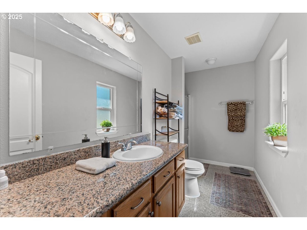 5122 Southeast Jenne Road Portland, OR 97236 - Photo 34 of 36 a bathroom with a granite countertop sink a toilet a mirror and shower