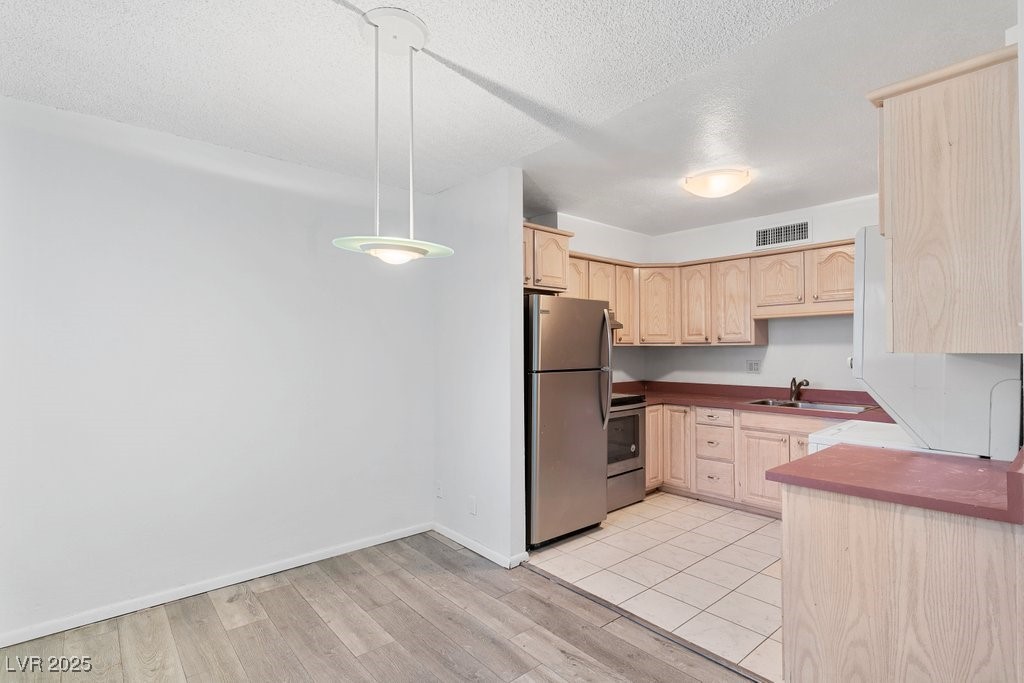 350 East Desert Inn Road, Unit H205 Las Vegas, NV 89109 - Photo 17 of 30 Kitchen with freestanding refrigerator, light brown cabinetry, a textured ceiling, stove, and light wood-style flooring