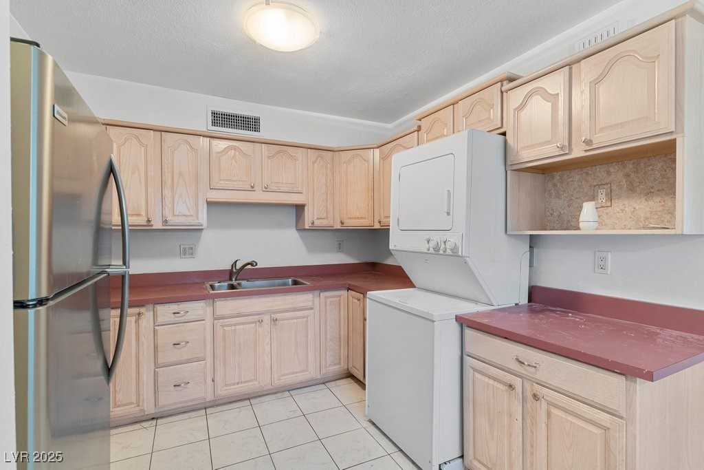350 East Desert Inn Road, Unit H205 Las Vegas, NV 89109 - Photo 20 of 30 Kitchen with freestanding refrigerator, light brown cabinets, stacked washer / drying machine, light tile patterned floors, and open shelves
