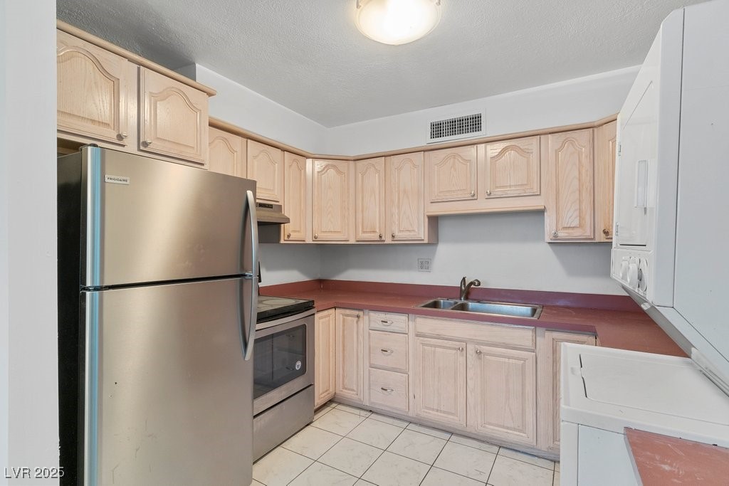 350 East Desert Inn Road, Unit H205 Las Vegas, NV 89109 - Photo 8 of 30 Kitchen with stainless steel appliances, under cabinet range hood, light brown cabinets, light tile patterned flooring, and a textured ceiling