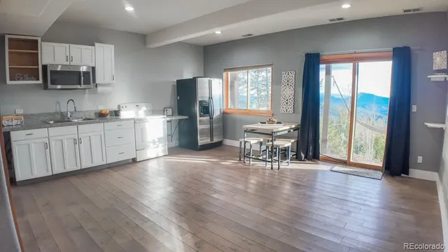 a kitchen with stainless steel appliances granite countertop a stove top oven a sink dishwasher a dining table and chairs with wooden floor