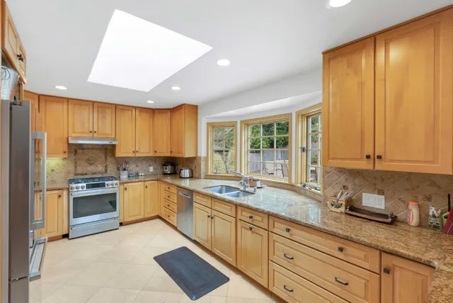 a kitchen with stainless steel appliances granite countertop a stove a sink dishwasher and a refrigerator with wooden cabinets