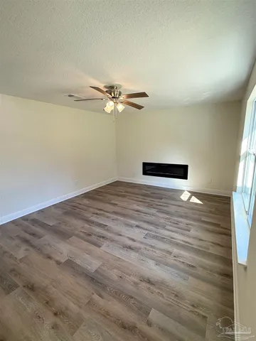 an empty room with wooden floor fan and windows
