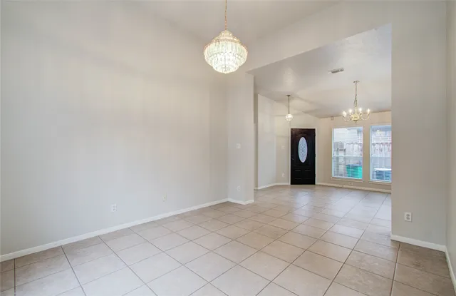 an empty room with kitchen and a chandelier fan