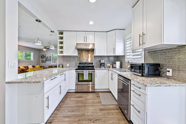 a kitchen with granite countertop a stove top oven a sink dishwasher white cabinets and wooden floor