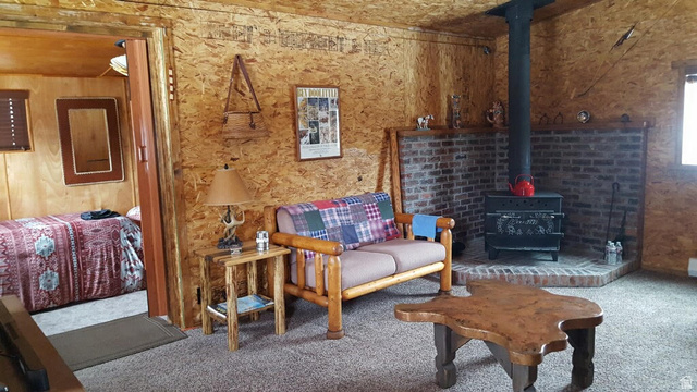 2006 Swenson Valley Road Bancroft, ID 83217 - Photo 38 of 51 Living area featuring wood paneling, a brick-surround wood-burning stove with a metal flue, and carpeting