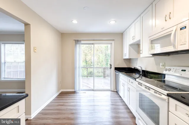 a kitchen with stainless steel appliances granite countertop a stove a sink and white cabinets with wooden floor