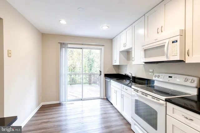 a kitchen with stainless steel appliances granite countertop a stove a sink and white cabinets with wooden floor