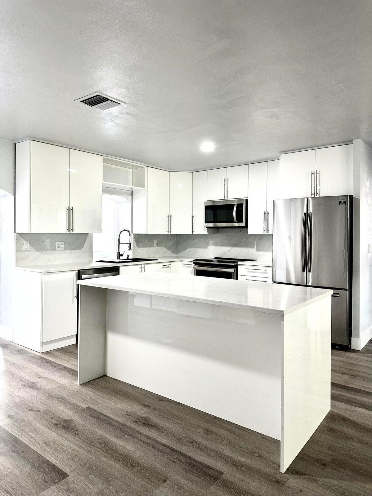 1455 Northeast Silver Maple Way Jensen Beach, FL 34957 - Photo 15 of 55 a kitchen with stainless steel appliances granite countertop a refrigerator a stove a sink and white cabinets with wooden floor