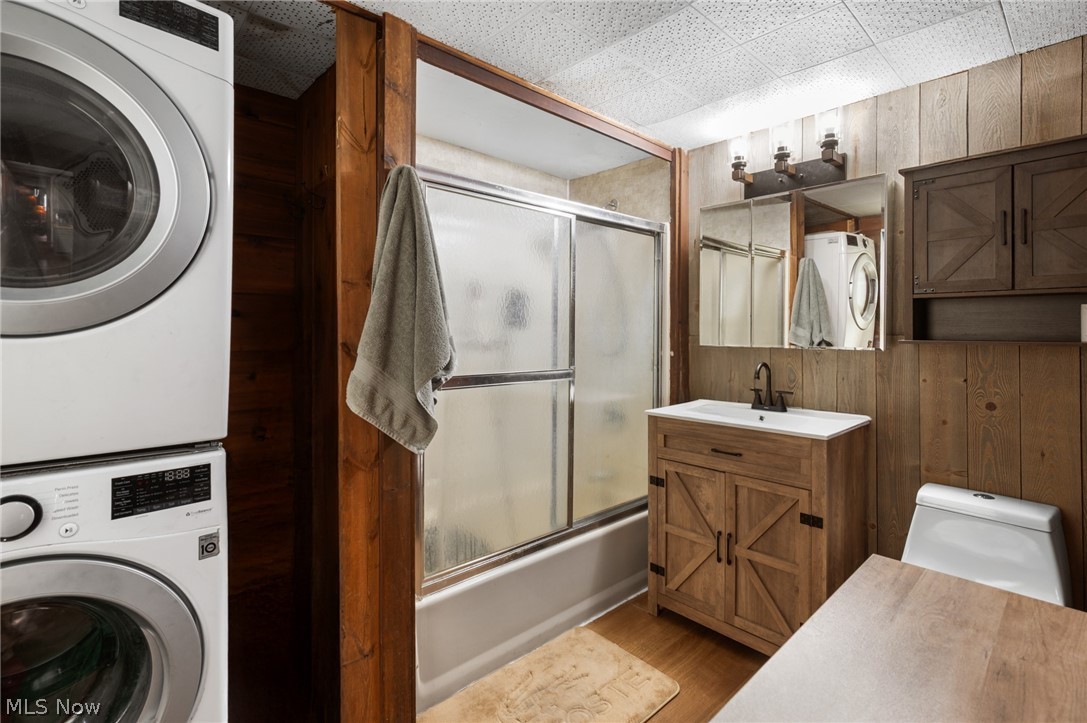 9455 Robinson Road Chardon, OH 44024 - Photo 18 of 33 Bathroom featuring wooden walls, bath / shower combo with glass door, vanity, stacked washing machine and dryer, and light wood-style floors