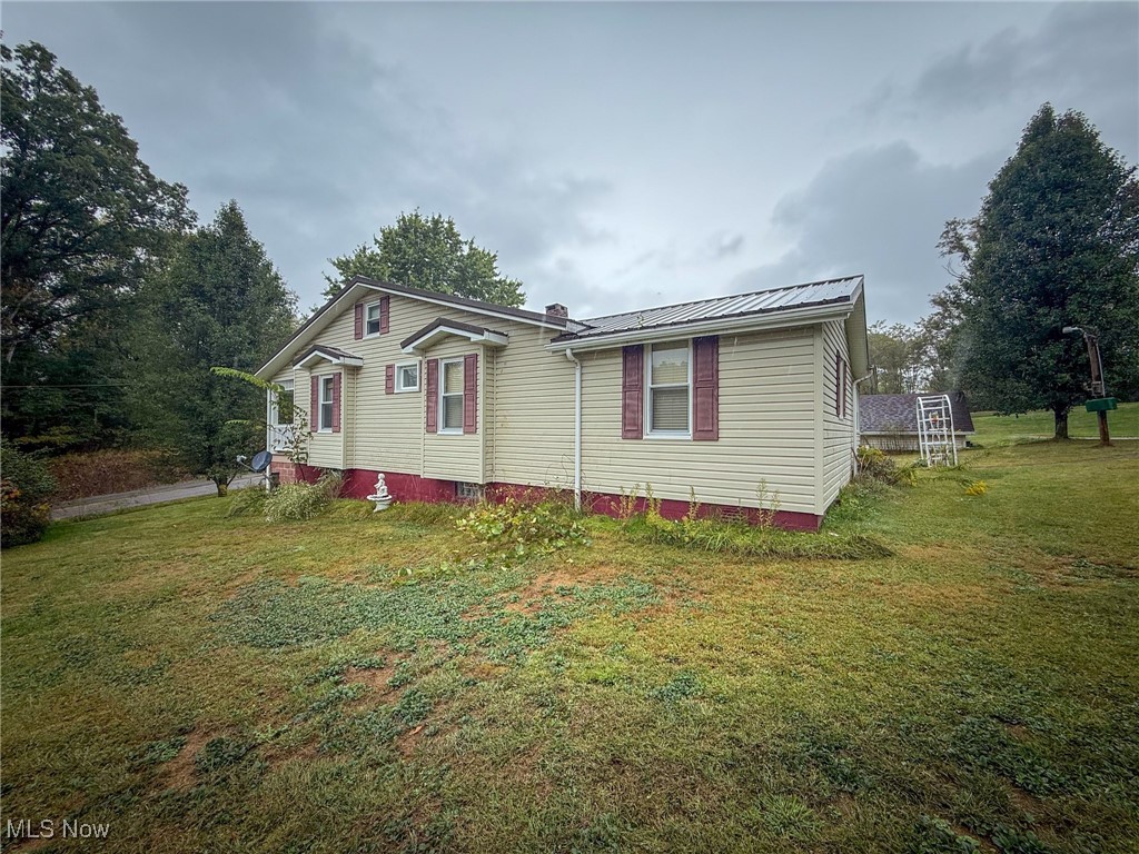 View of property exterior with a lawn, a metal roof, and a chimney