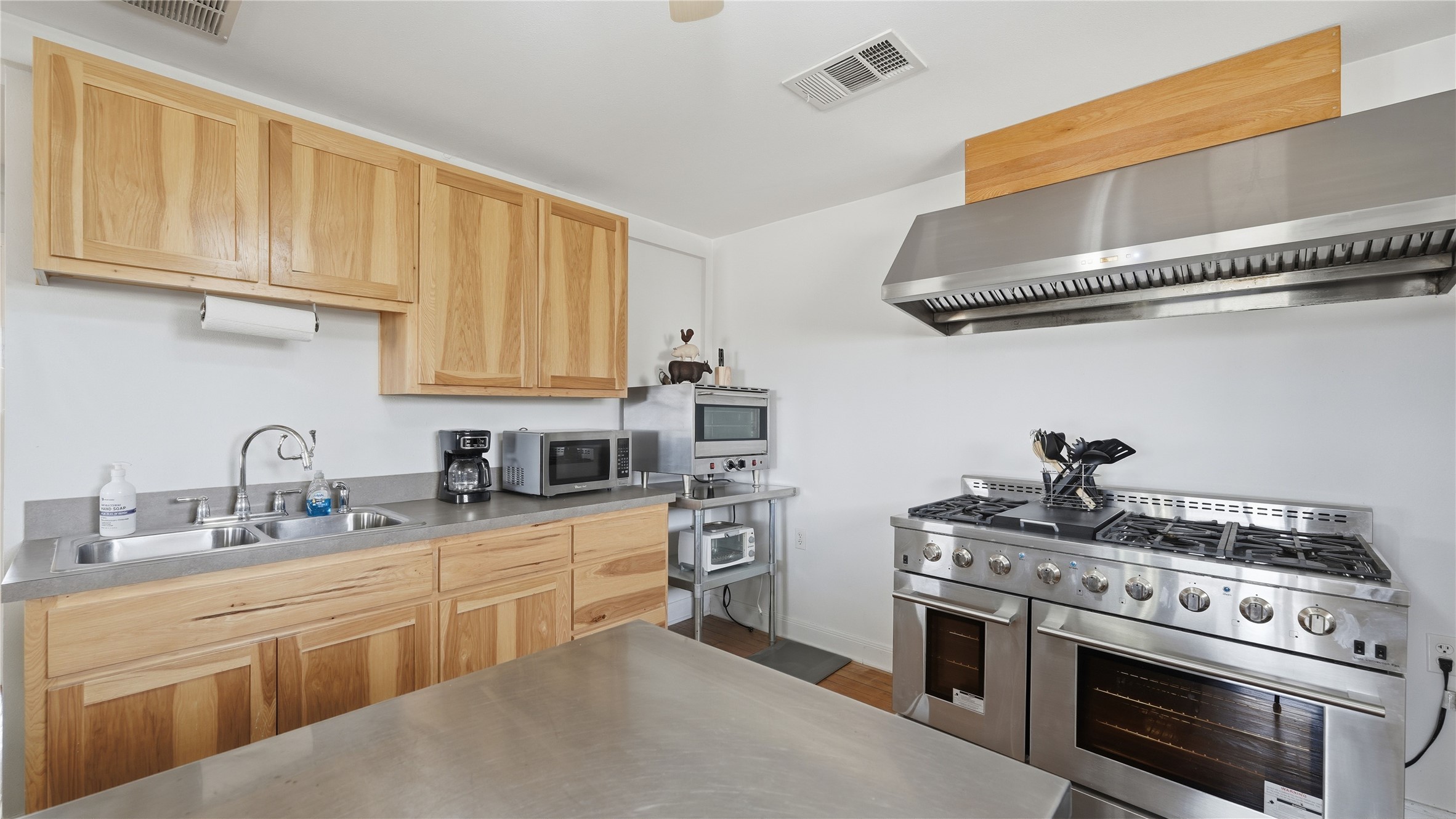 218 Little Ranch Road, Unit E Red Rock, TX 78662 - Photo 7 of 22 Kitchen featuring stainless steel appliances, light wood finish cabinets, stainless steel counters, and dark wood finished floors
