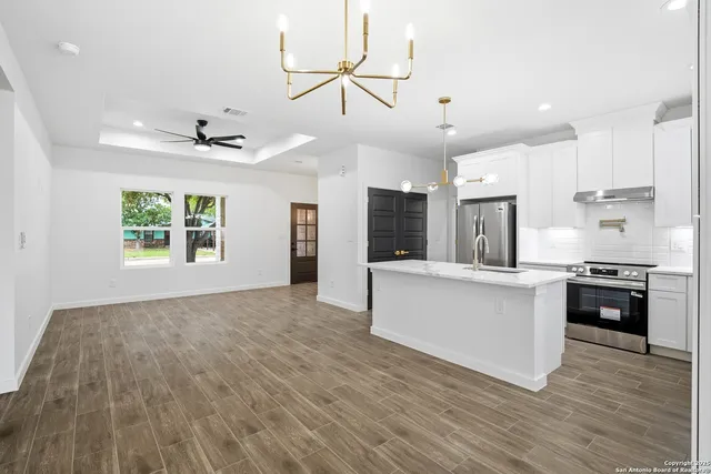 a large white kitchen with kitchen island a stove a sink dishwasher and a oven with wooden floor