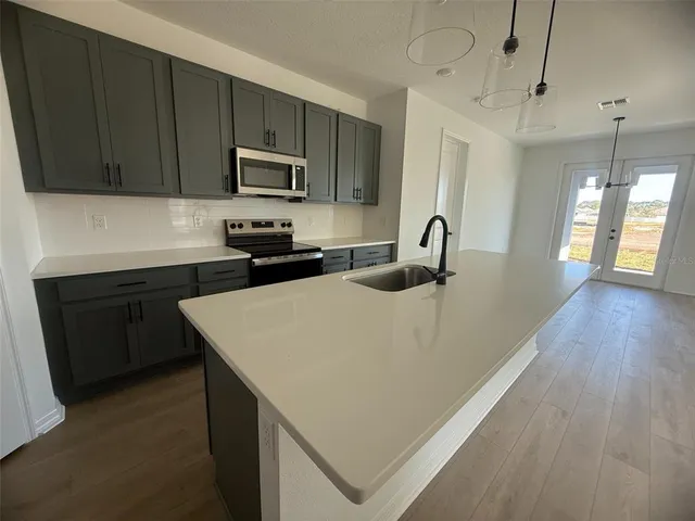 a kitchen with stainless steel appliances a sink dishwasher a refrigerator a stove top oven a large island with wooden floor and cabinets