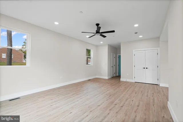 a view of an empty room with wooden floor and a ceiling fan