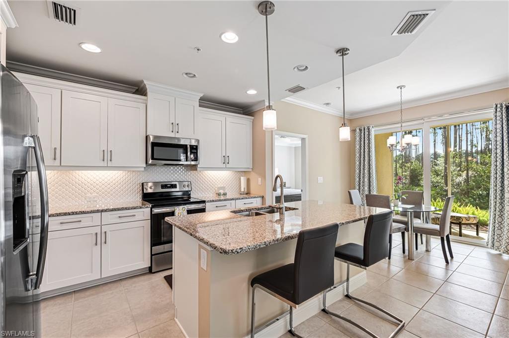 6969 Avalon Circle, Unit 1504 Naples, FL 34112 - Photo 15 of 42 a kitchen with stainless steel appliances granite countertop a stove a sink a microwave a dining table and chairs