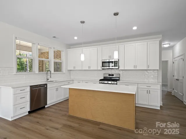 a kitchen with stainless steel appliances granite countertop a stove a sink dishwasher a refrigerator white cabinets and wooden floor next to a window