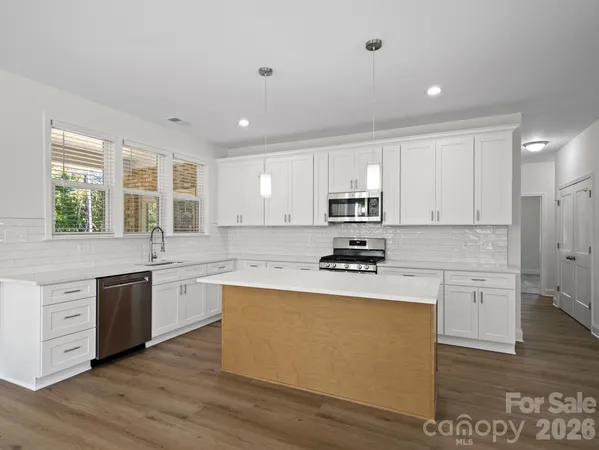 a kitchen with stainless steel appliances granite countertop a stove a sink dishwasher a refrigerator white cabinets and wooden floor next to a window