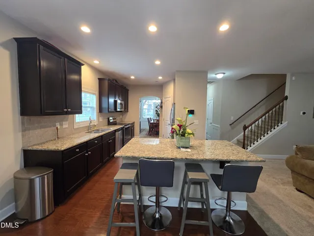 a large kitchen with granite countertop a dining table chairs wooden cabinets and stainless steel appliances