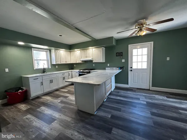 a large white kitchen with kitchen island a stove a sink dishwasher and a fireplace with wooden floor