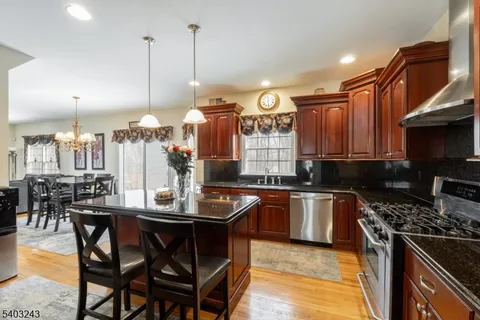 a kitchen with stainless steel appliances granite countertop a stove top oven a sink a dining table and chairs with wooden floor