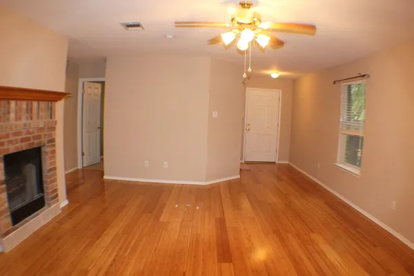 a view of an empty room with wooden floor fireplace and a window