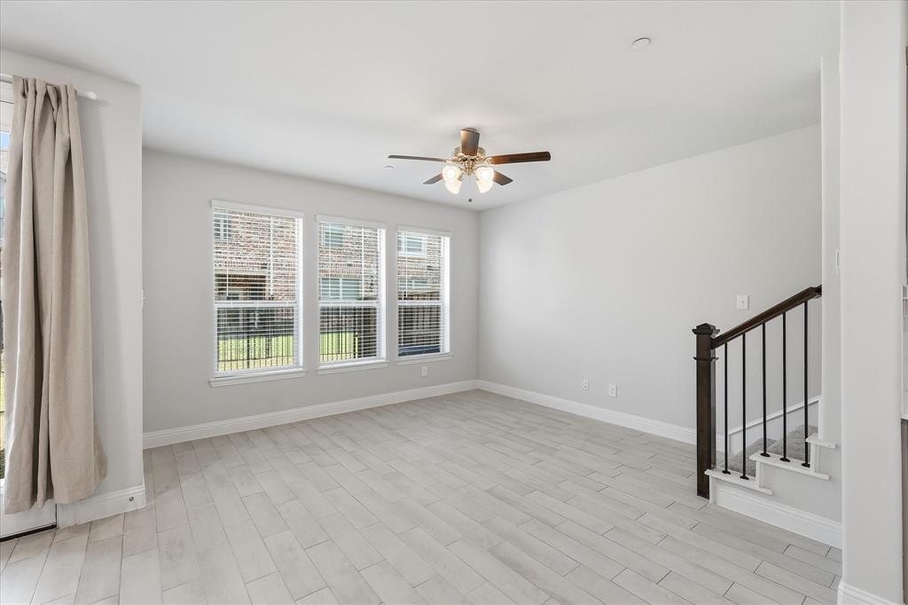 519 Sequoia Street Allen, TX 75002 - Photo 8 of 38 Spacious room featuring light wood-finish flooring, three windows with white blinds, a ceiling fan with integrated lighting, and a white door with glass paneling leading to an outdoor area with a wooden fence