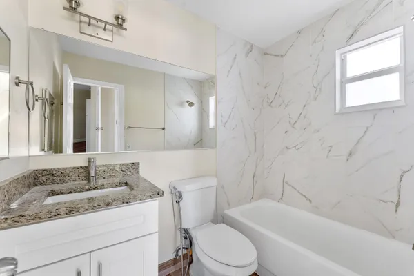 a bathroom with a granite countertop sink toilet mirror and bathtub