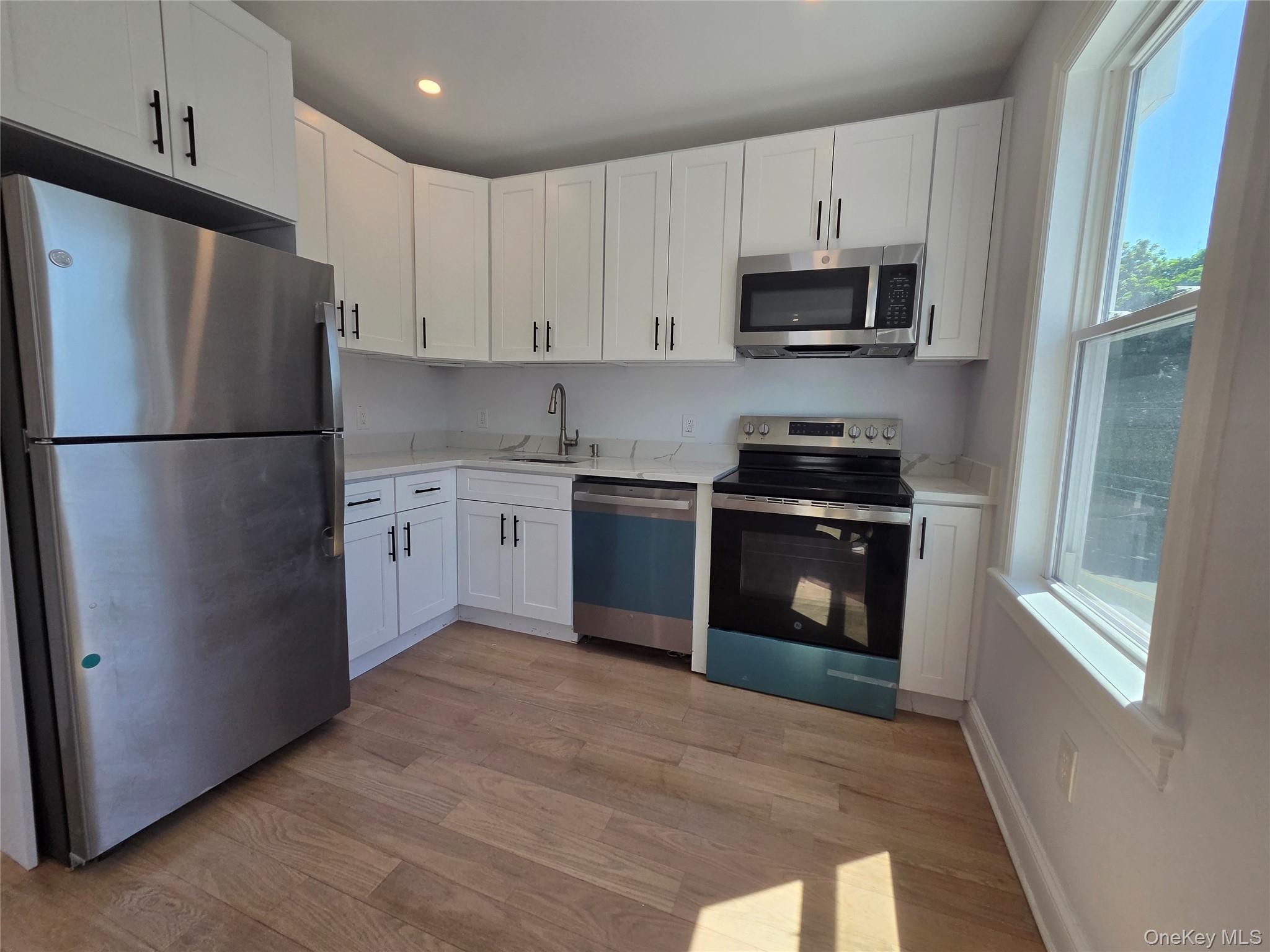 965 Main Street, Unit 2 New Rochelle, NY 10801 - Photo 4 of 12 Modern kitchen featuring white shaker cabinetry, stainless steel appliances, light-toned countertops, and wood-finish flooring