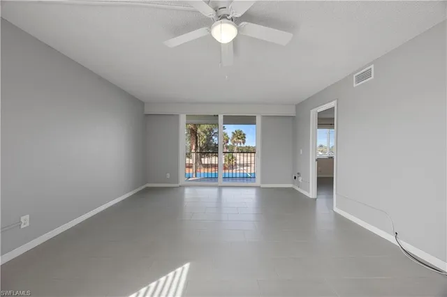 an empty room with chandelier fan and windows