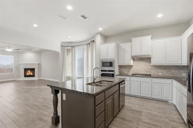 a kitchen with stainless steel appliances granite countertop a stove top oven a sink dishwasher and a refrigerator with wooden floor