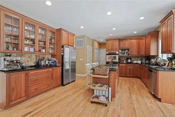 a kitchen with stainless steel appliances granite countertop a refrigerator a stove top oven a sink dishwasher and wooden cabinets with wooden floor