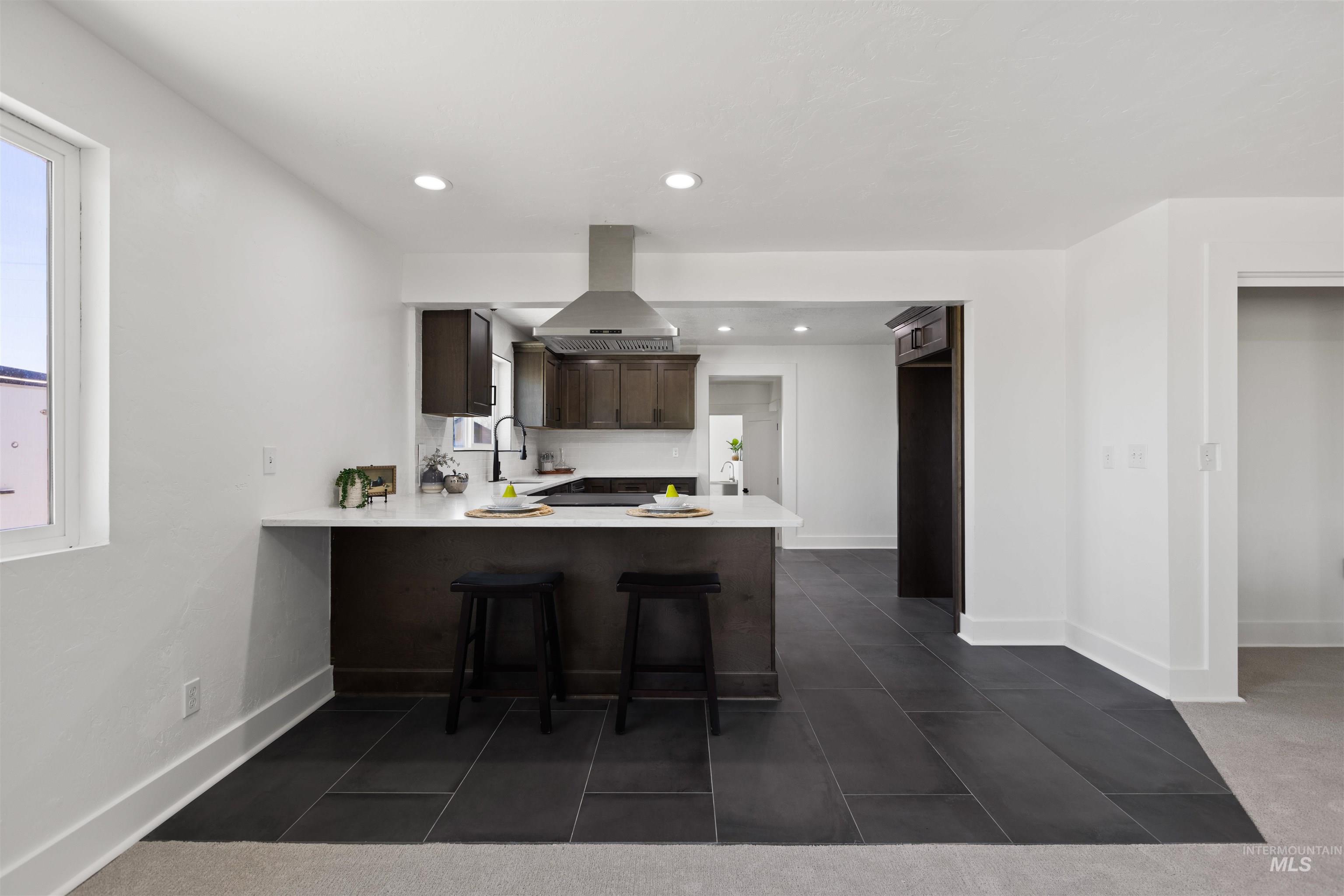 29862 Emmett Road Caldwell, ID 83607 - Photo 30 of 44 Kitchen featuring a peninsula, a kitchen breakfast bar, dark wood finish cabinets, exhaust hood, and dark tile patterned floors