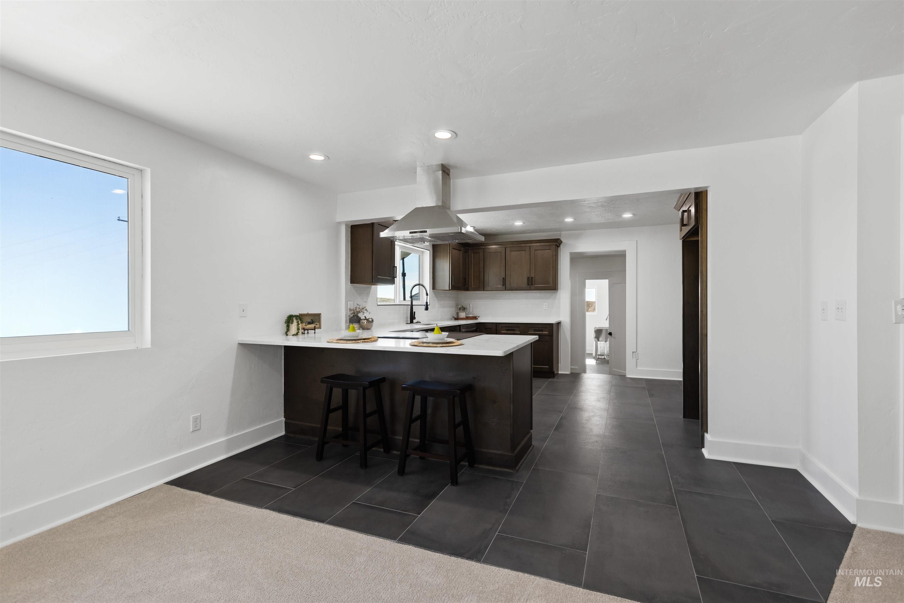 29862 Emmett Road Caldwell, ID 83607 - Photo 31 of 44 Kitchen with a peninsula, dark wood finish cabinetry, a breakfast bar area, island range hood, and dark tile patterned flooring