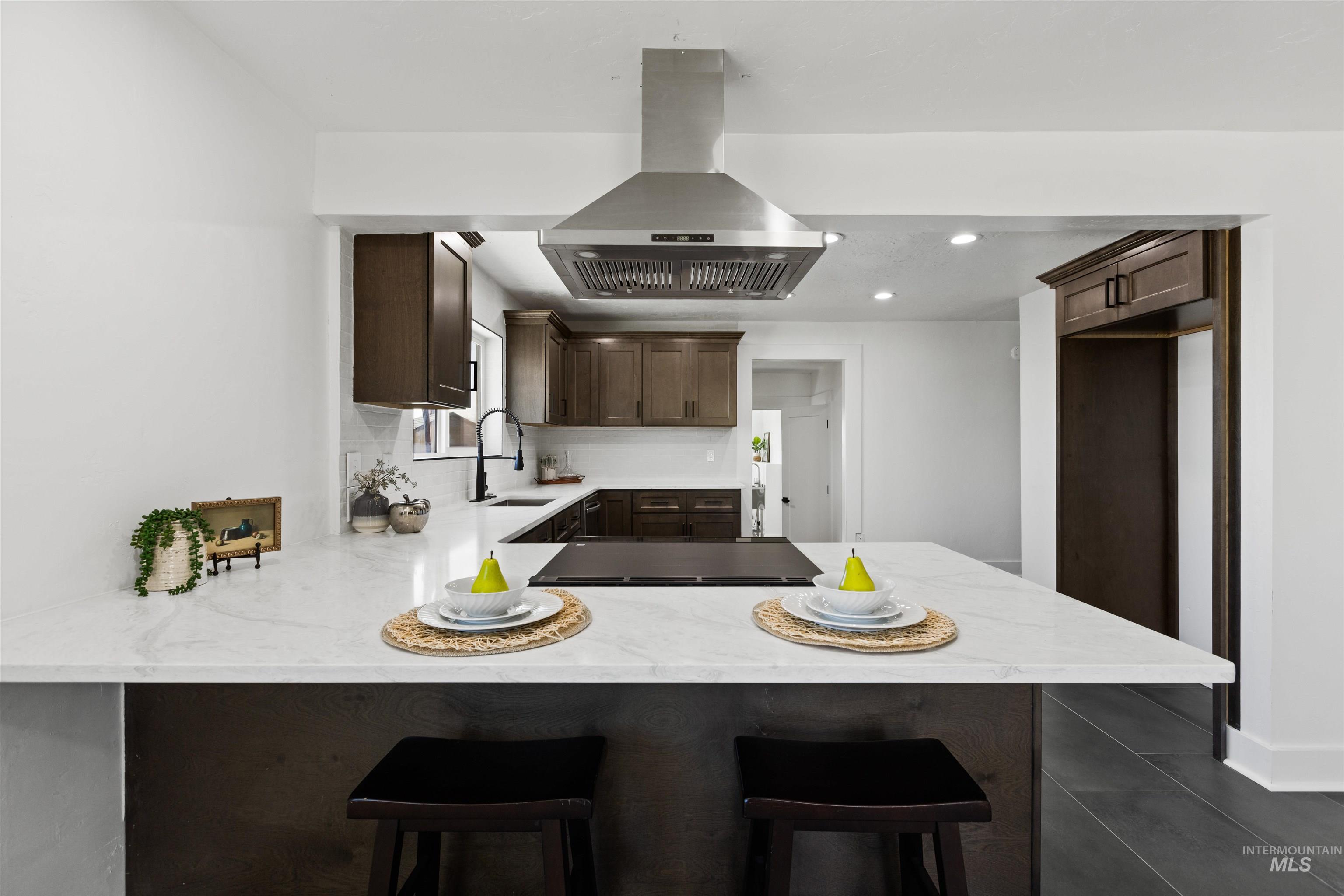 29862 Emmett Road Caldwell, ID 83607 - Photo 32 of 44 Kitchen with dark wood finish cabinets, island range hood, light stone countertops, recessed lighting, and a kitchen breakfast bar