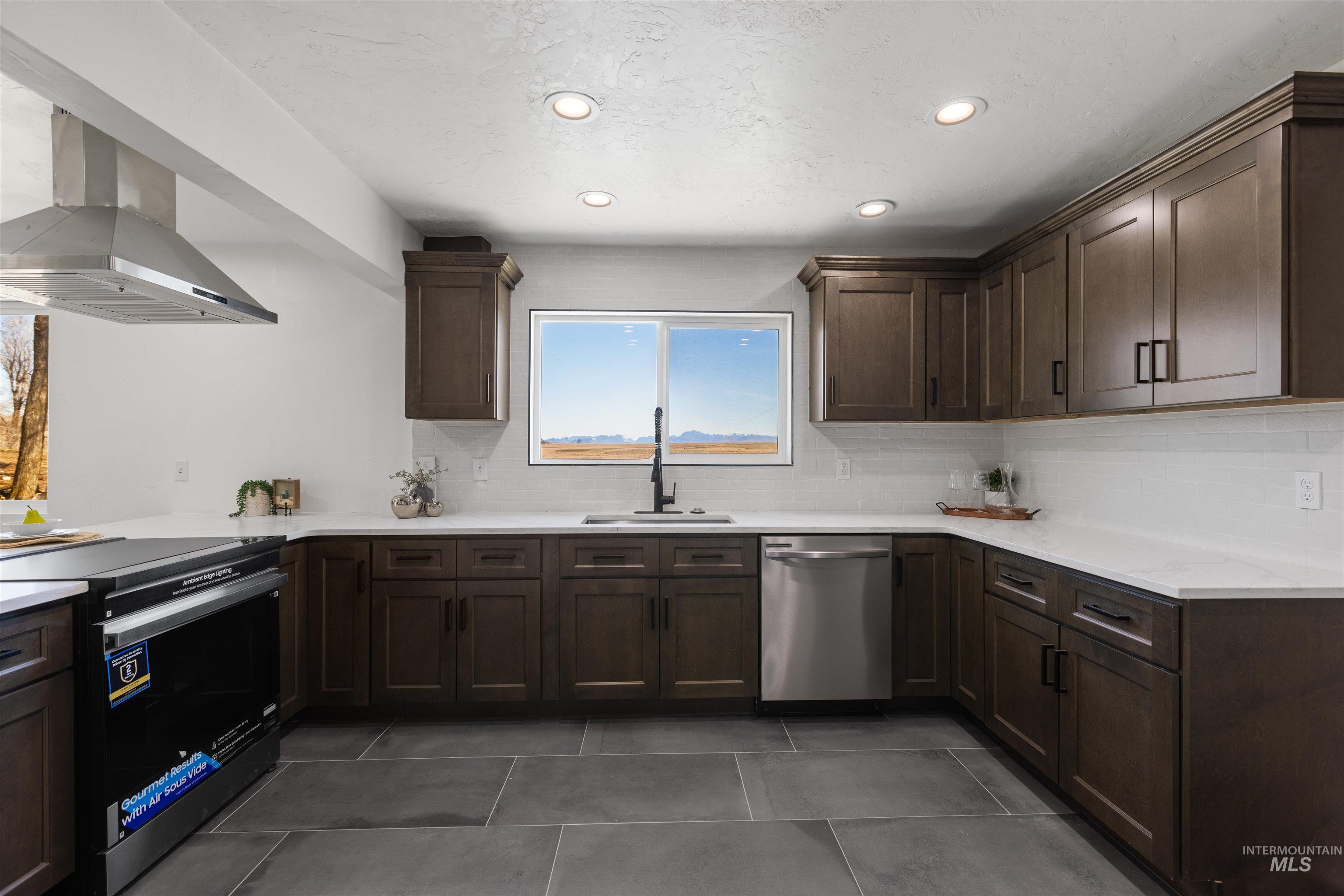 29862 Emmett Road Caldwell, ID 83607 - Photo 34 of 44 Kitchen featuring dark wood finish cabinetry, range, island range hood, stainless steel dishwasher, and backsplash
