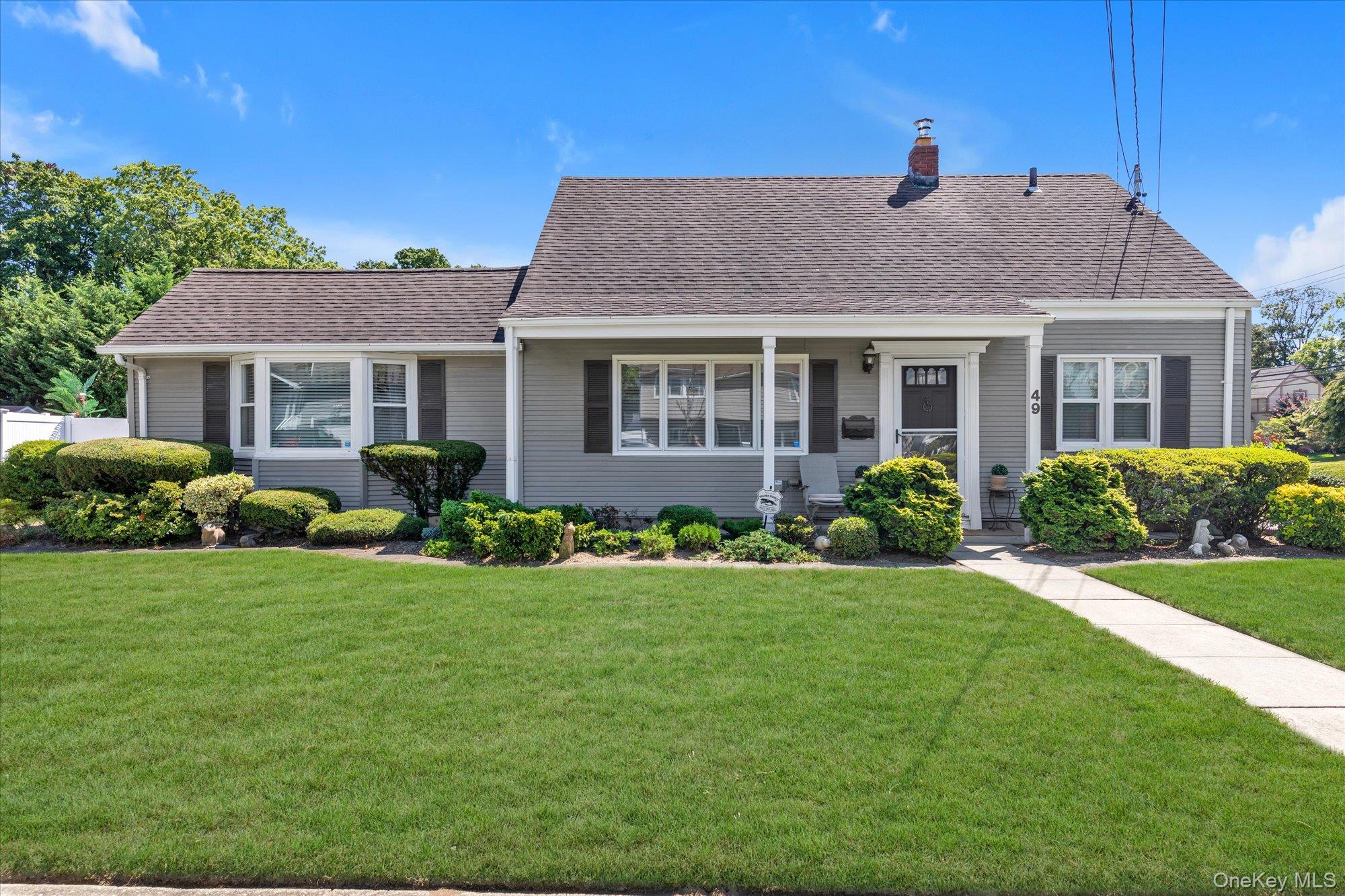 View of front of house with a front lawn, a chimney, a shingled roof, and a porch