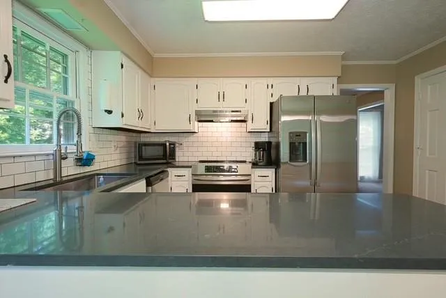 a kitchen with stainless steel appliances granite countertop a stove a refrigerator a sink and white cabinets with wooden floor