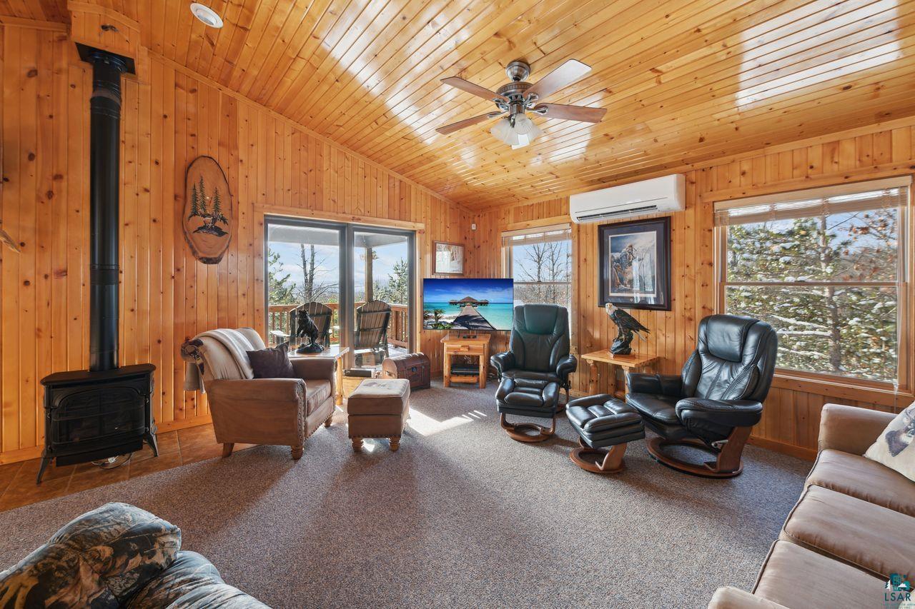 28255 Friendly Valley Road Washburn, WI 54891 - Photo 4 of 34 Carpeted living room with a wood stove, vaulted ceiling, ceiling fan, wood ceiling, and a wall unit AC