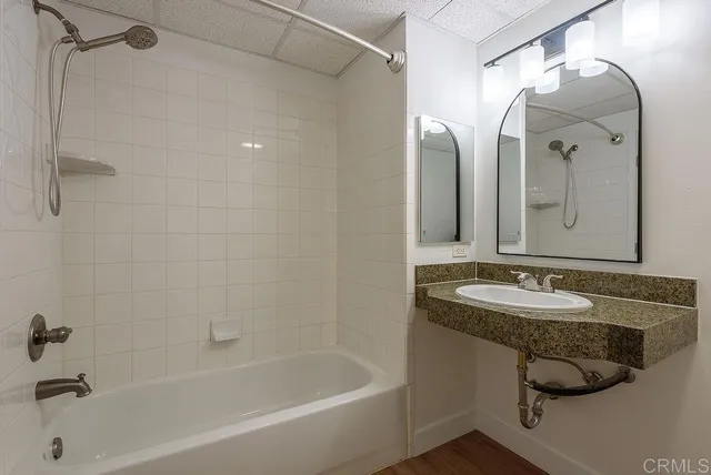 a bathroom with a granite countertop sink a mirror a bathtub and shower
