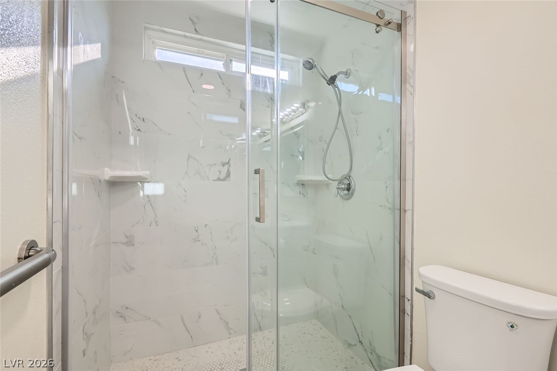 3665 Bronco Road Las Vegas, NV 89103 - Photo 16 of 28 Modern marble-patterned tile lines this walk-in shower with a sleek glass enclosure.
