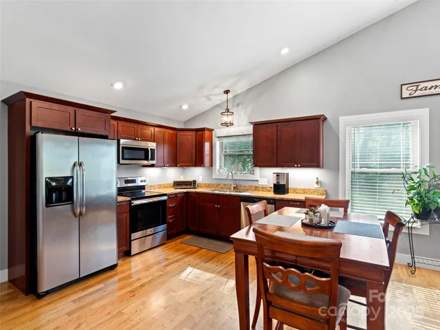 a large kitchen with stainless steel appliances kitchen island granite countertop a refrigerator a stove a sink a dining table and chairs with wooden floor