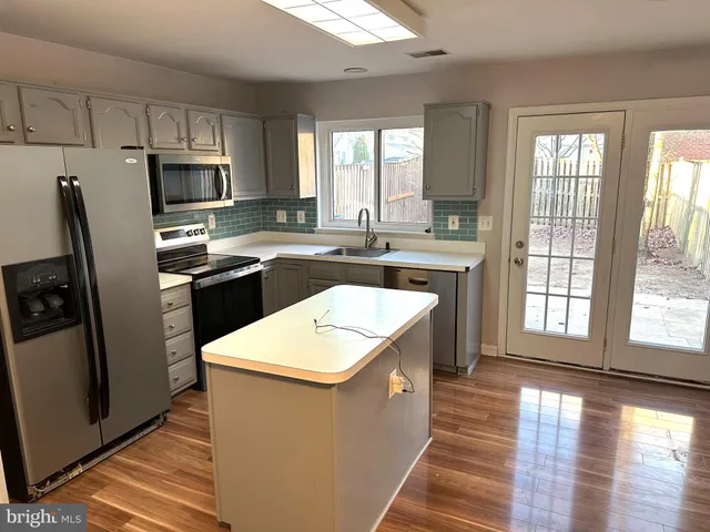 a kitchen with stainless steel appliances granite countertop a refrigerator a sink dishwasher a stove and white countertops with wooden floor