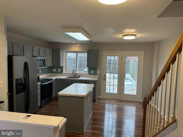 a kitchen with stainless steel appliances granite countertop a refrigerator a sink dishwasher a stove and white countertops with wooden floor