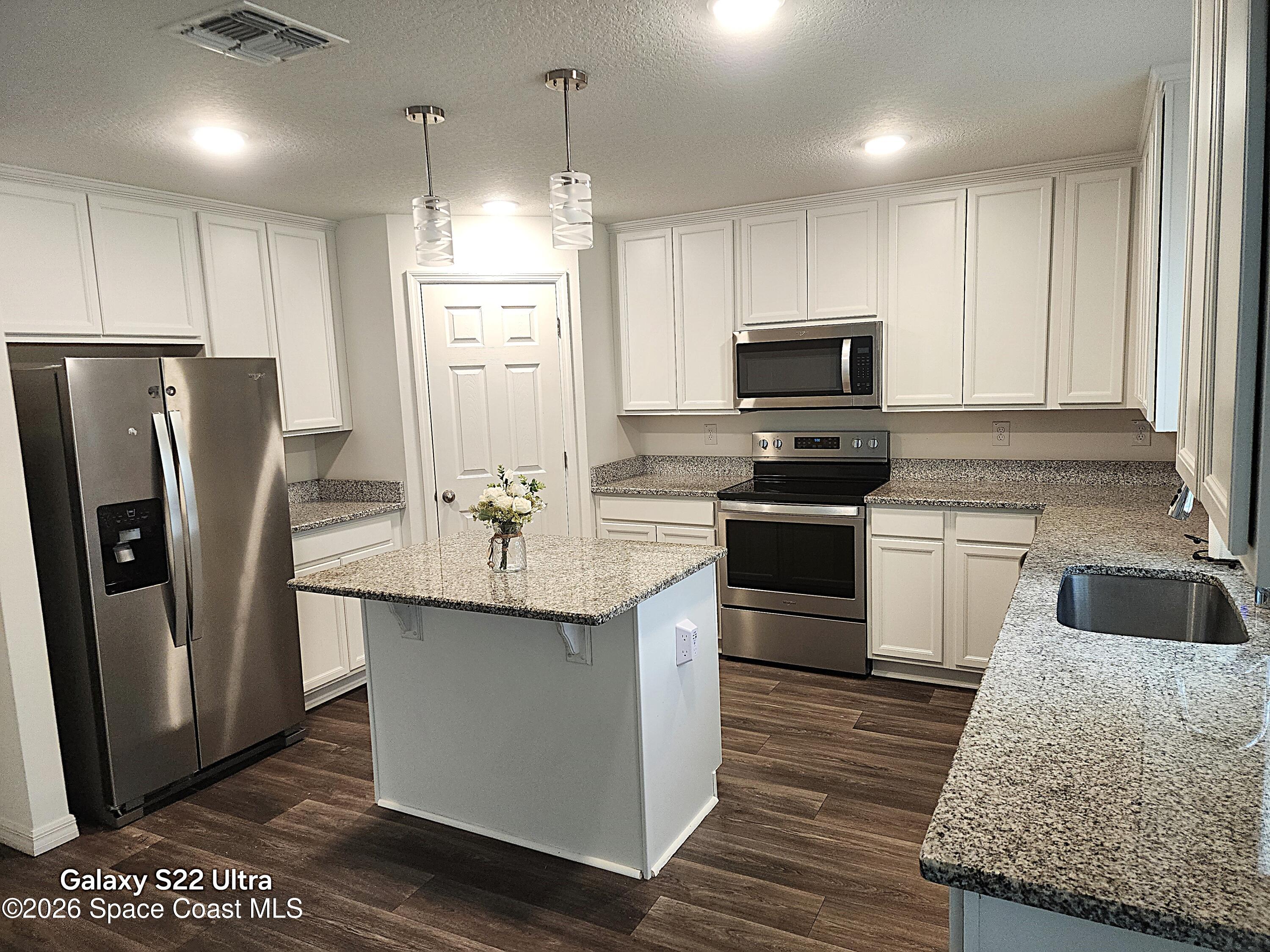 1043 Corbin Circle Southwest Palm Bay, FL 32908 - Photo 7 of 18 a kitchen with granite countertop a refrigerator a sink a stove a microwave and island